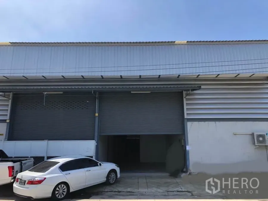 Warehouse for rent in Mueang Samut Prakan, Samut Prakan - Industrial warehouse frontage with large metal roller shutter and parking area.