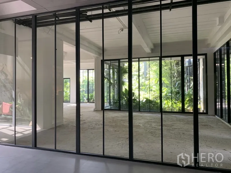 办公空间 出租在Khlong Toei, Bangkok - 玻璃立面后的日照办公区，花园背景与外露梁
