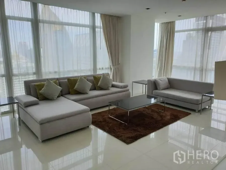 Condominium for rent in Pathum Wan, Bangkok - Bright living room with floor-to-ceiling windows, grey sofas and a Bangkok city skyline view.