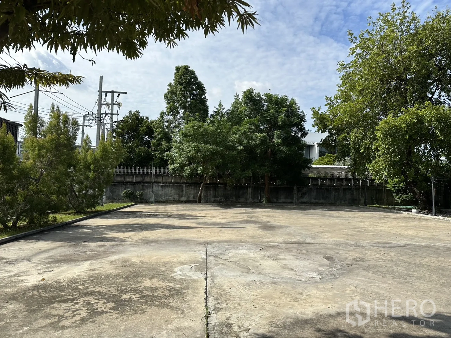 Warehouse for rent in Phra Khanong, Bangkok - Spacious open concrete yard bordered by trees and a perimeter wall.