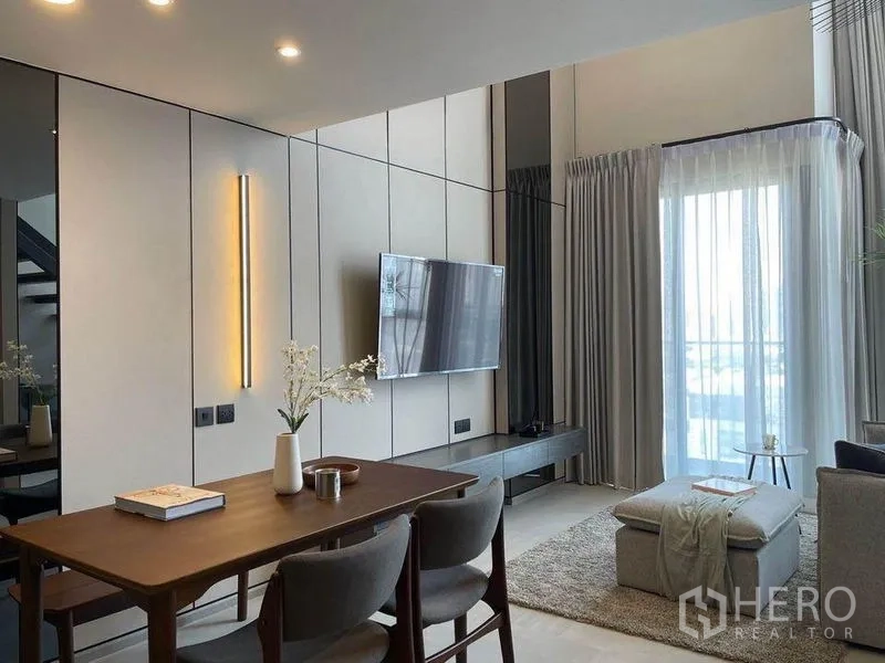 Condominium for rent in Pathum Wan, Bangkok - Dining table next to a modern kitchenette with lit open shelves, staircase and living zone beyond.