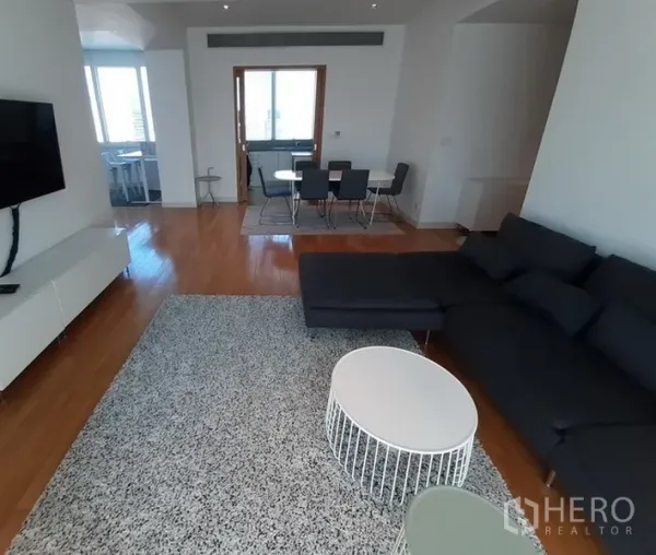 Condominium for rent in Khlong Toei, Bangkok - Open-plan lounge facing dining area with wall-mounted TV and large windows.