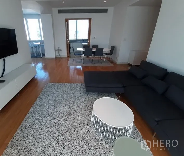 Condominium for rent in Khlong Toei, Bangkok - Open-plan lounge facing dining area with wall-mounted TV and large windows.