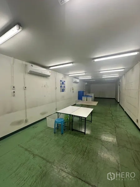 Warehouse for rent or sale in Lam Luk Ka, Pathum Thani - Long workroom with tables, air‑conditioning units and green floor for assembly tasks.