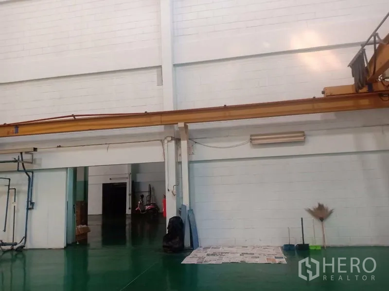 Factory for sale in Khlong Luang, Pathum Thani - Interior wall with crane rail system and wide doorway to storage area.