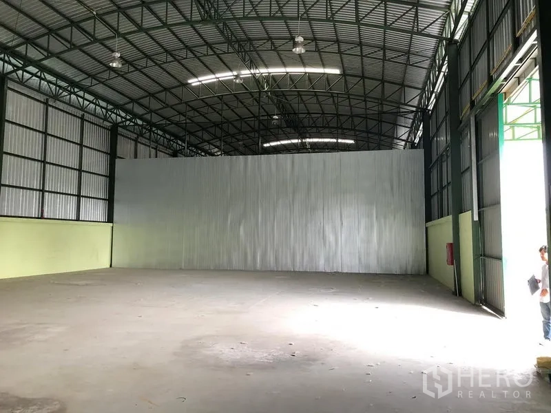 Warehouse for rent in Lat Krabang, Bangkok - Interior view toward a partition wall with large side doors, concrete flooring, and a wall-mounted fire extinguisher.