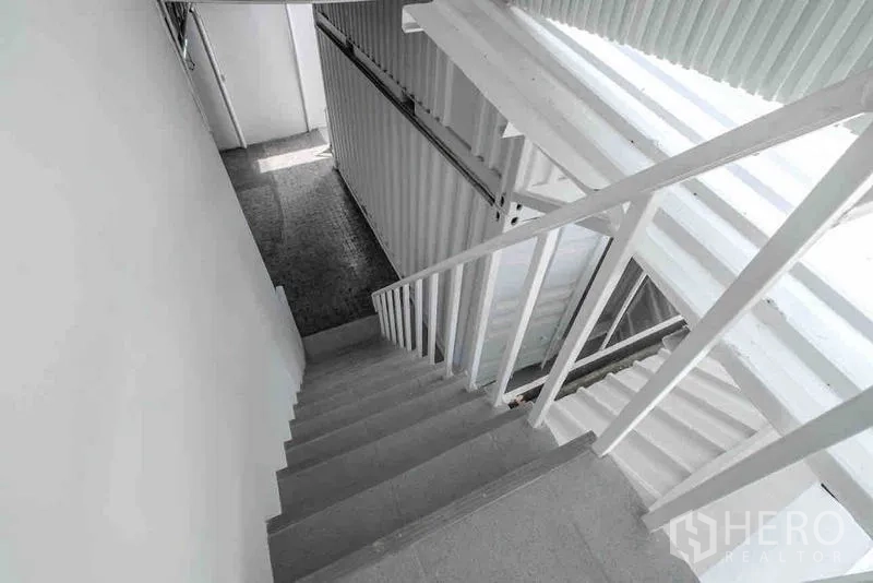 Standalone for rent or sale in Bang Na, Bangkok - White metal staircase leading to upper levels and roof under a skylight roof.