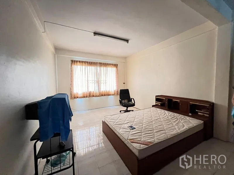 Shophouse for sale in Phra Khanong, Bangkok - Spacious bedroom with large window, tiled floor, bed base and office chair.