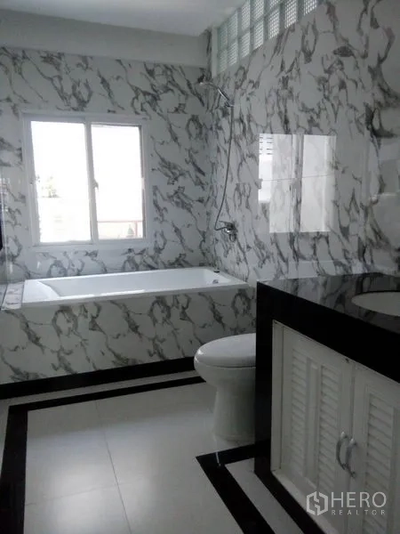 Townhouse for sale in Khlong Toei, Bangkok - Bathroom with marble-pattern walls, bathtub, window, and black stone vanity.