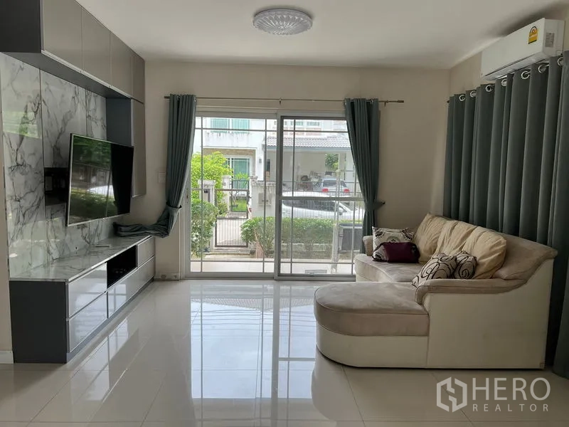Detached House for rent in Bang Kapi, Bangkok - Bright living room with marble-feature TV wall, sectional sofa, and sliding glass doors to the patio.