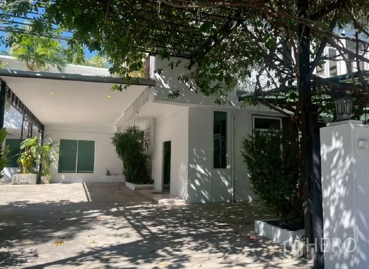 Home Office for rent in Watthana, Bangkok - Front facade with shaded entry, large windows and planters beneath leafy trees.