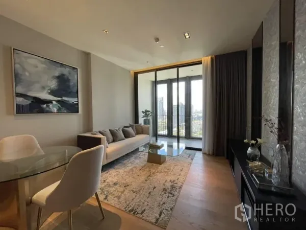 Condominium for rent in Khlong Toei, Bangkok - Living and dining area with wood flooring, glass coffee table, large windows, and skyline outlook.
