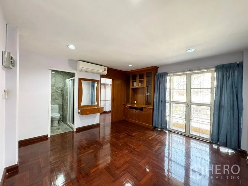 Townhouse for rent or sale in Suan Luang, Bangkok - Master bedroom with built-in wood cabinetry, balcony doors and ensuite access
