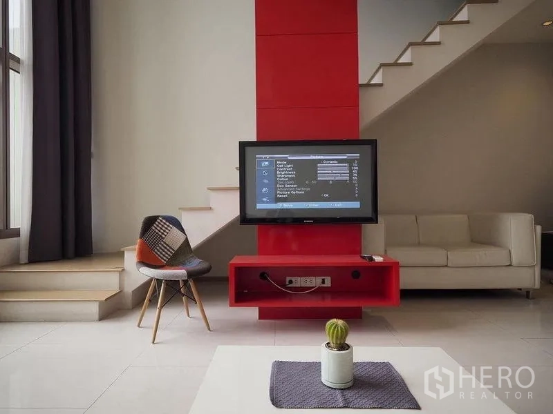 Condominium for rent in Khlong Toei, Bangkok - Modern duplex living room with red TV wall, floating stairs and a large window.
