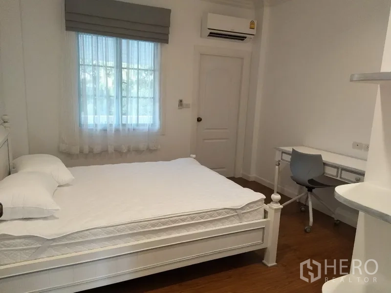 Townhouse for rent in Mueang Samut Prakan, Samut Prakan - Light-filled bedroom with white bed, study desk, and air conditioning.