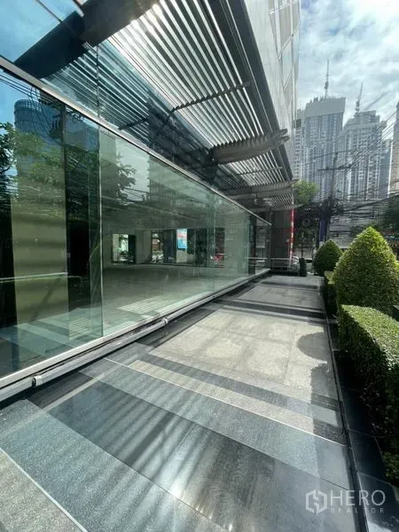 Retail Space for rent in Watthana, Bangkok - Exterior walkway with glass facade, louvered canopy and trimmed hedges in a city setting.