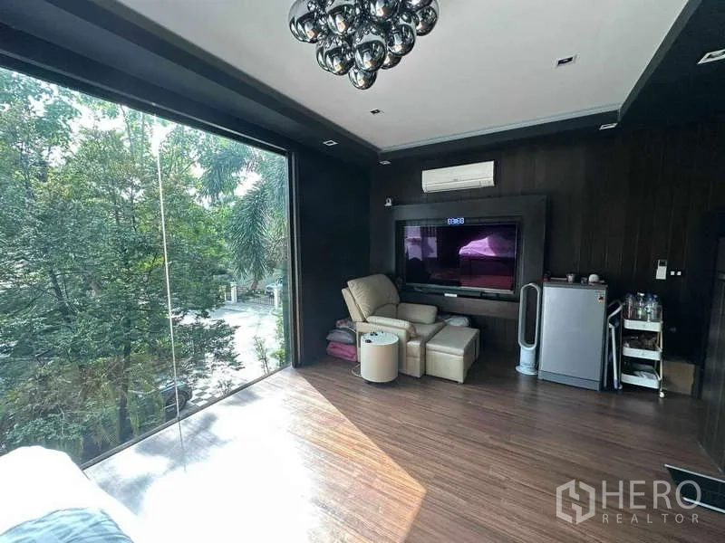 Detached House for sale in Suan Luang, Bangkok - Master suite corner with large TV, recliner, mini fridge and a wide glass window to greenery.