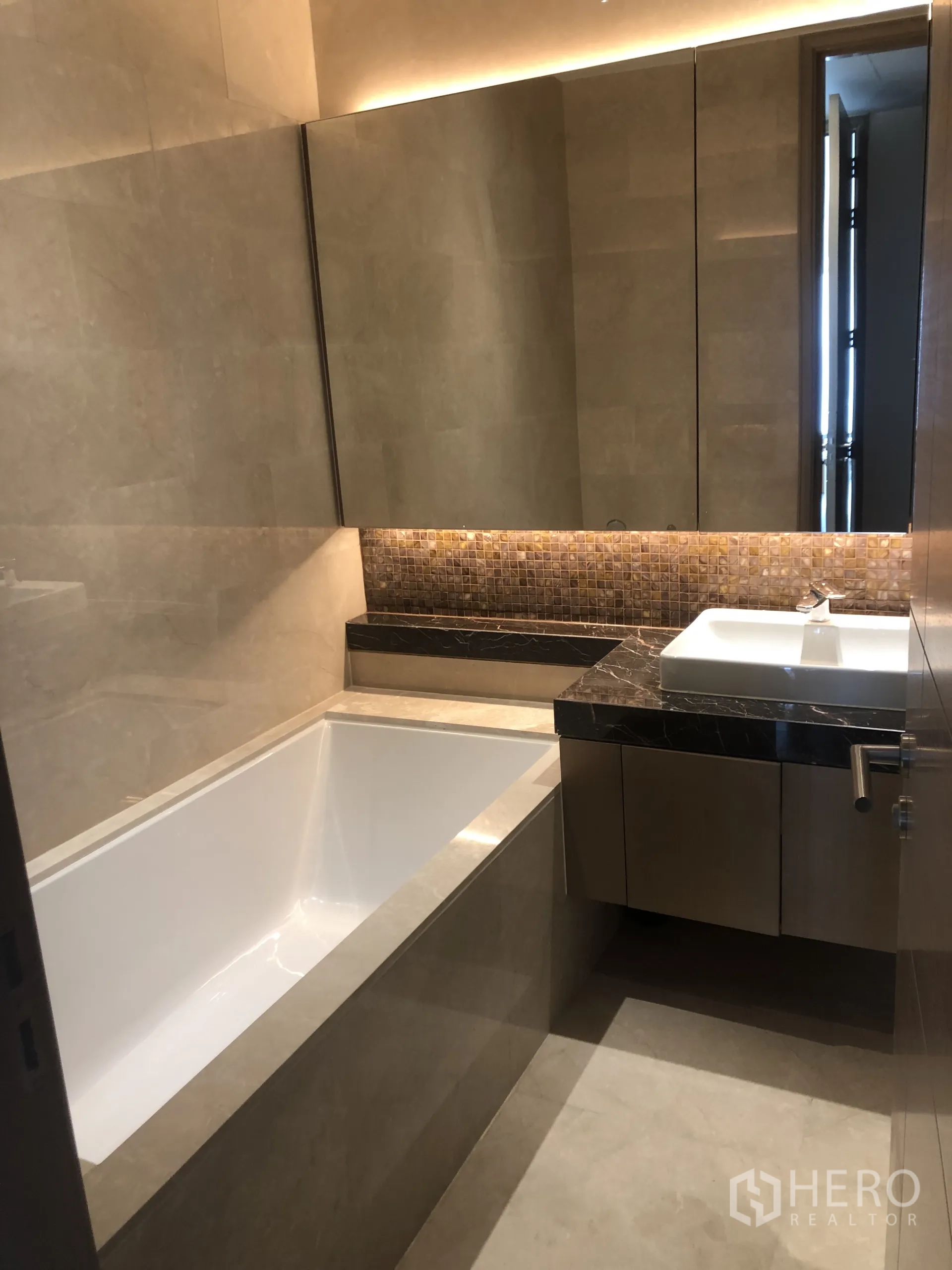 Condominium for rent in Pathum Wan, Bangkok - Bathroom with deep soaking tub, marble vanity and large mirrored cabinets with ambient lighting.