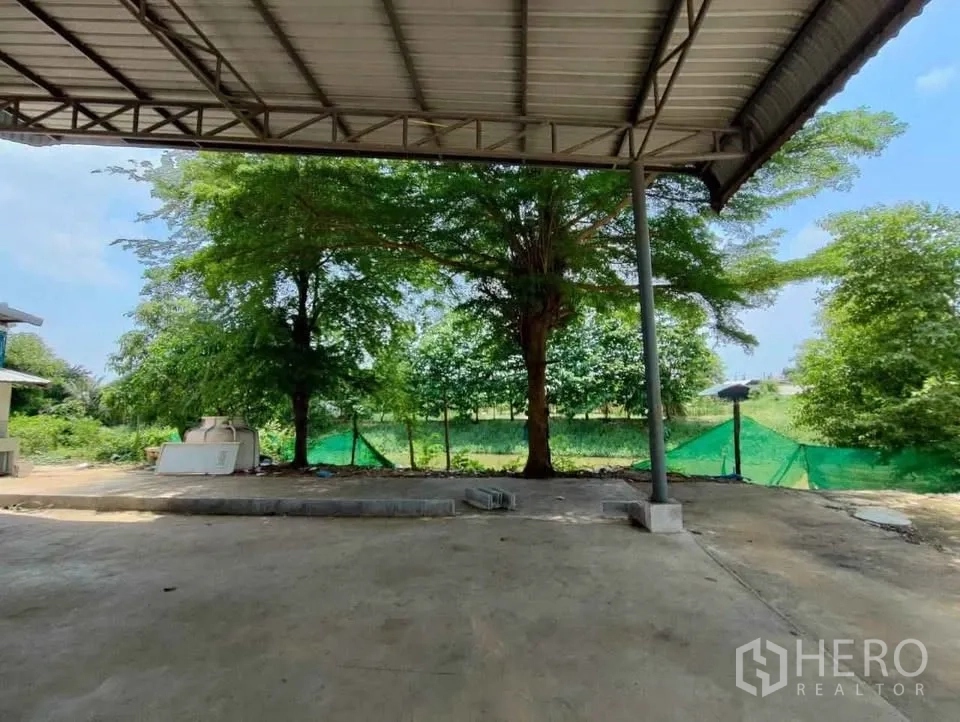 工厂 出租在Mueang Chachoengsao, Chachoengsao - 带顶雨棚与开阔院子，面向绿树的地块边界。