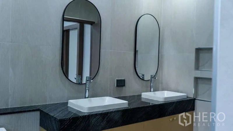 Detached House for rent or sale in Suan Luang, Bangkok - Double vanity with oval mirrors and dark stone countertop in a modern bathroom