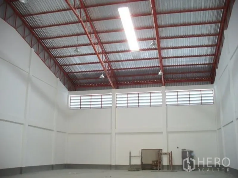 工厂 出租或出售在Samut Prakan - 仓库内部高挑红钢桁架屋顶，带高侧窗通风与充足照明。