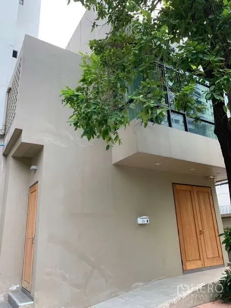 Detached House for rent - Modern two-storey facade with timber doors and large corner windows shaded by a tree.