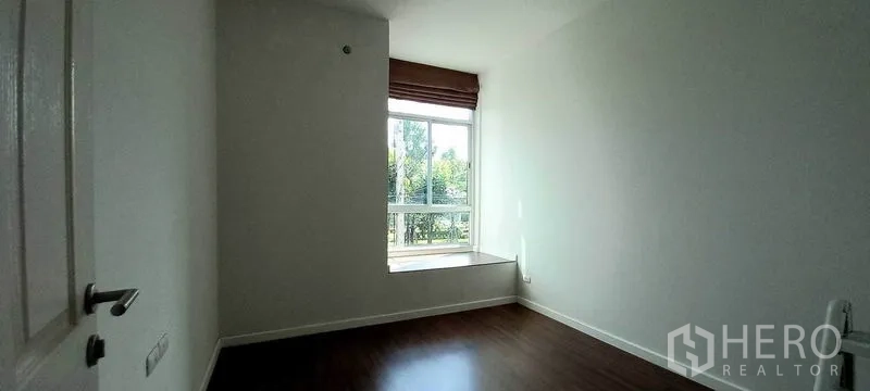 Townhouse for sale in Mueang Pathum Thani, Pathum Thani - Cozy bedroom with large window seat and garden views, wood laminate flooring.