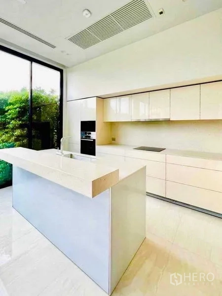 Detached House for sale in Huai Khwang, Bangkok - Minimalist kitchen with island, built-in appliances and a tall window to greenery.