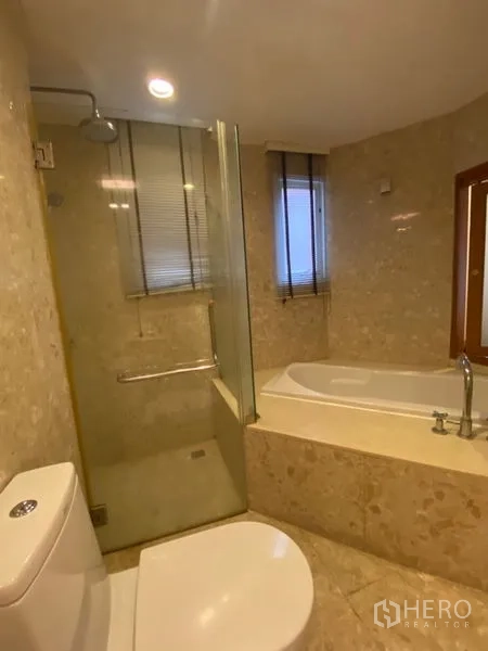 Condominium for rent in Watthana, Bangkok - Ensuite bathroom with glass shower, built-in bathtub, and beige marble-style tiling.