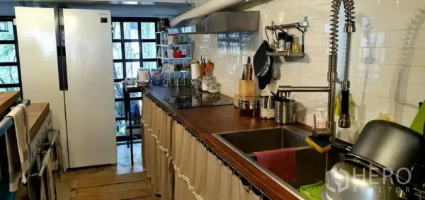 Townhouse for rent in Khlong Toei, Bangkok - Modern galley kitchen with wood countertops, white subway tiles, open shelving, large fridge and pull-down faucet.
