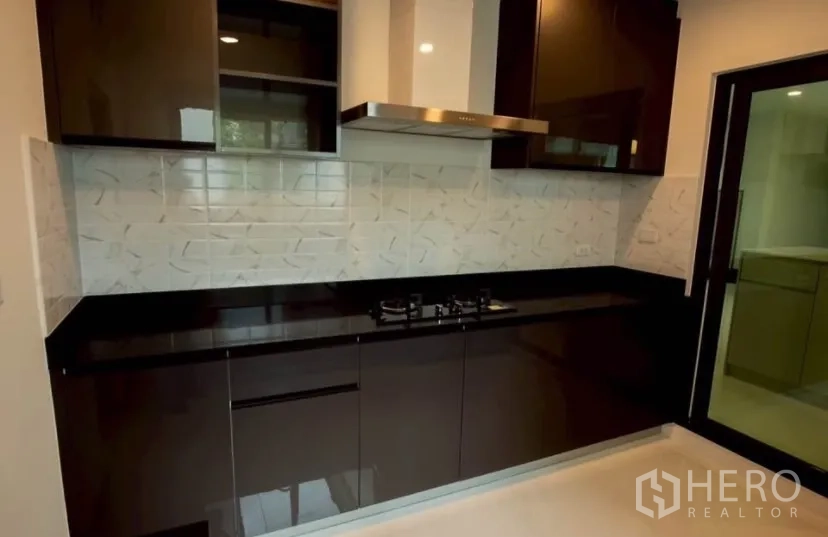 Detached House for rent in Bang Phli, Samut Prakan - Sleek Western kitchen with black cabinetry, gas cooktop, stainless hood and tiled backsplash.