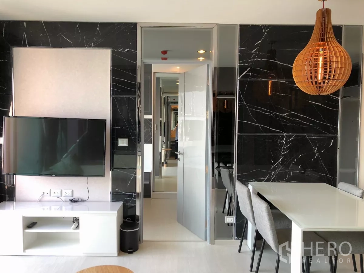 Condominium for rent in Khlong Toei, Bangkok - Living room with wall-mounted TV on black marble feature wall and dining table.