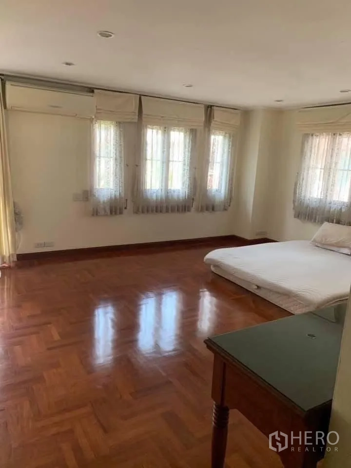 Townhouse for rent in Watthana, Bangkok - Spacious bedroom with wood floors, multiple windows, air conditioner and a mattress.