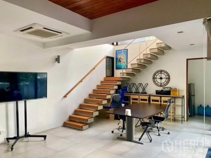 Townhouse for rent in Khlong Toei, Bangkok - Open-plan living area with floating wooden staircase and workspace.