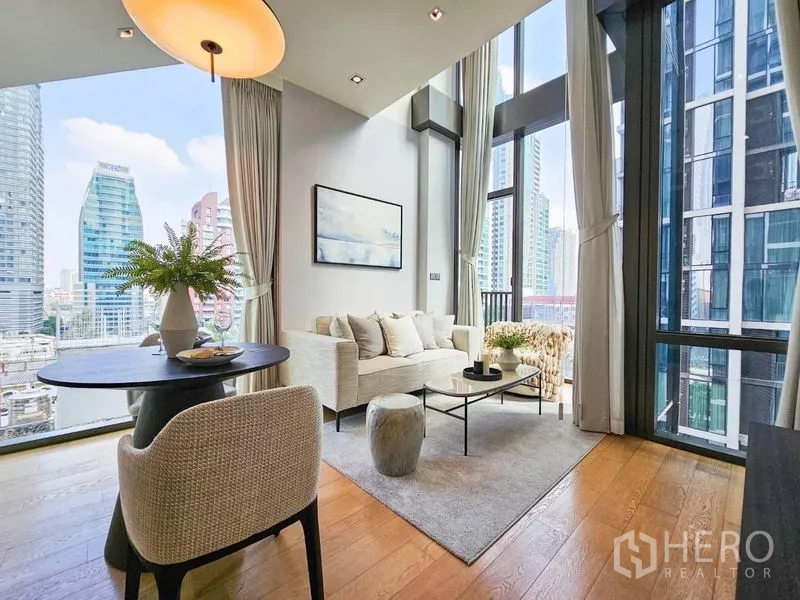 Condominium for rent - Bright living room with double-height windows, sofa, and city view in a Pathum Wan condo.