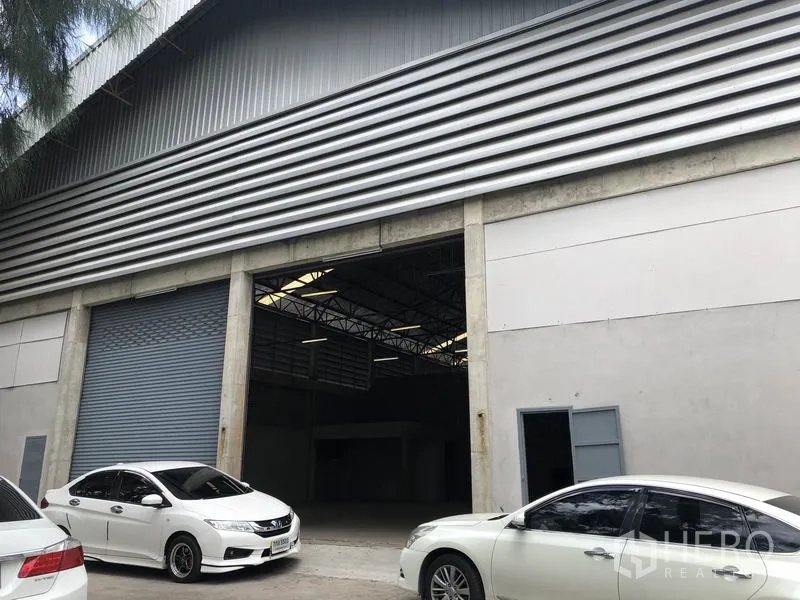 Warehouse for rent in Khlong Sam Wa, Bangkok - Front facade close-up of the warehouse with two big roller shutters, a pedestrian door and parking spaces.