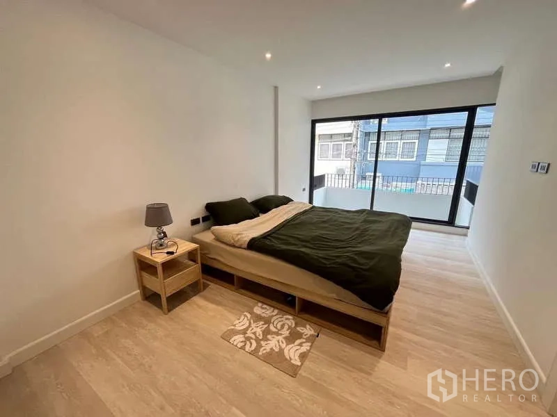 Townhouse for sale in Khlong Toei, Bangkok - Spacious bedroom with sliding glass doors opening to a balcony and wood-look floors.