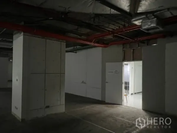 Office Space for rent - Dim interior corridor with structural columns, red fire lines, and an open door to a brighter lobby area.