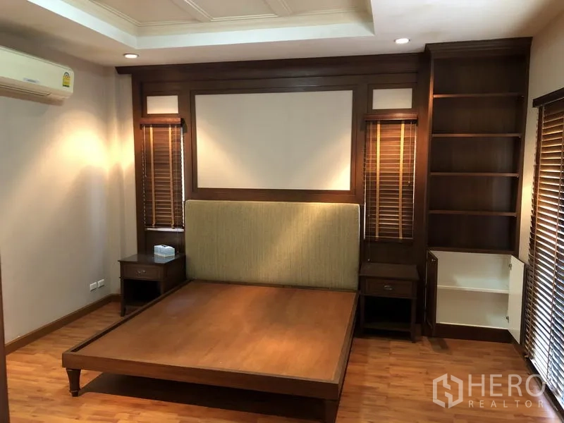 Detached House for rent or sale in Bang Kapi, Bangkok - Primary bedroom with built-in wood headboard, shelving and warm lighting.