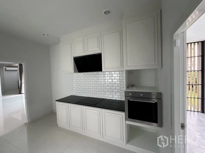 Detached House for sale in Lam Luk Ka, Pathum Thani - Built-in oven, cooktop and hood within a white paneled kitchen.