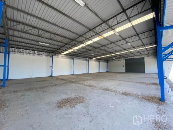 Factory for rent in Nonthaburi - Spacious factory interior with high metal roof, skylights, and a wide roller shutter door.