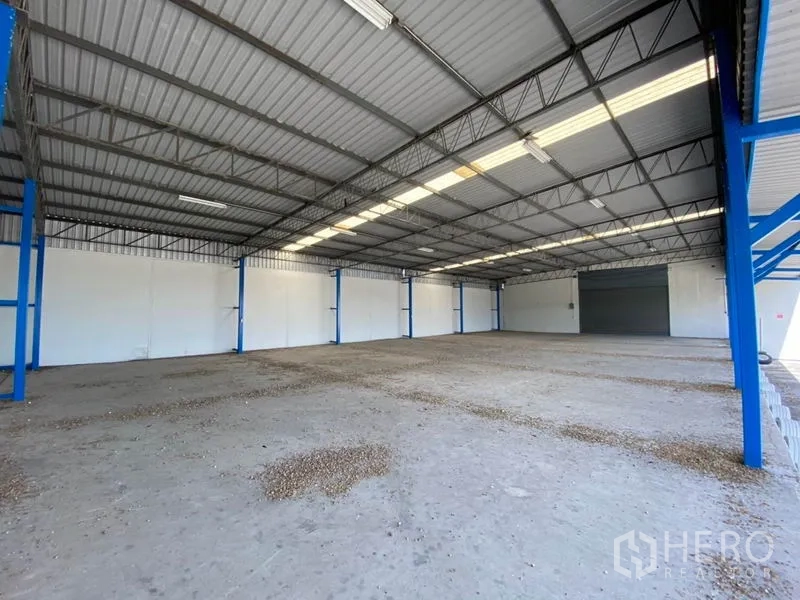 Factory for rent in Nonthaburi - Spacious factory interior with high metal roof, skylights, and a wide roller shutter door.