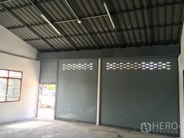 Warehouse for rent in Lam Luk Ka, Pathum Thani - Warehouse interior showing a high steel roof with fluorescent lighting and three roller-shutter loading bays.