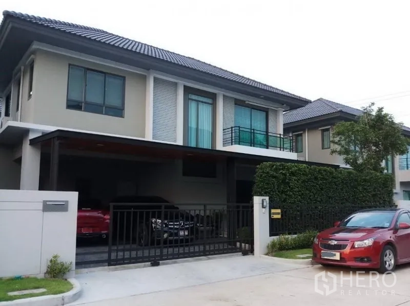 Detached House for sale in Nonthaburi - Modern two-storey detached house exterior with gated carport, balcony and manicured hedge.