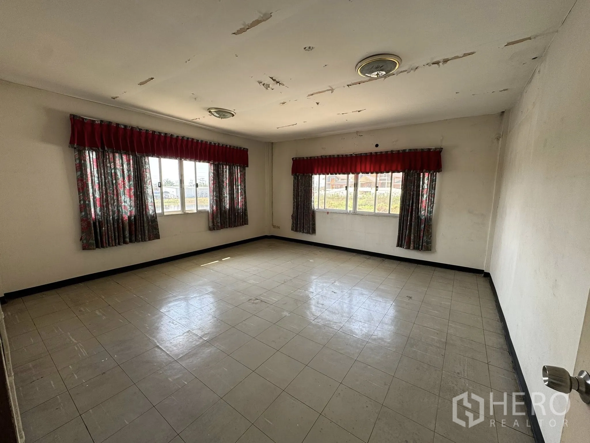 Warehouse for rent in Mueang Samut Sakhon, Samut Sakhon - Spacious empty office with tiled floor, large windows, red valances and a worn ceiling.