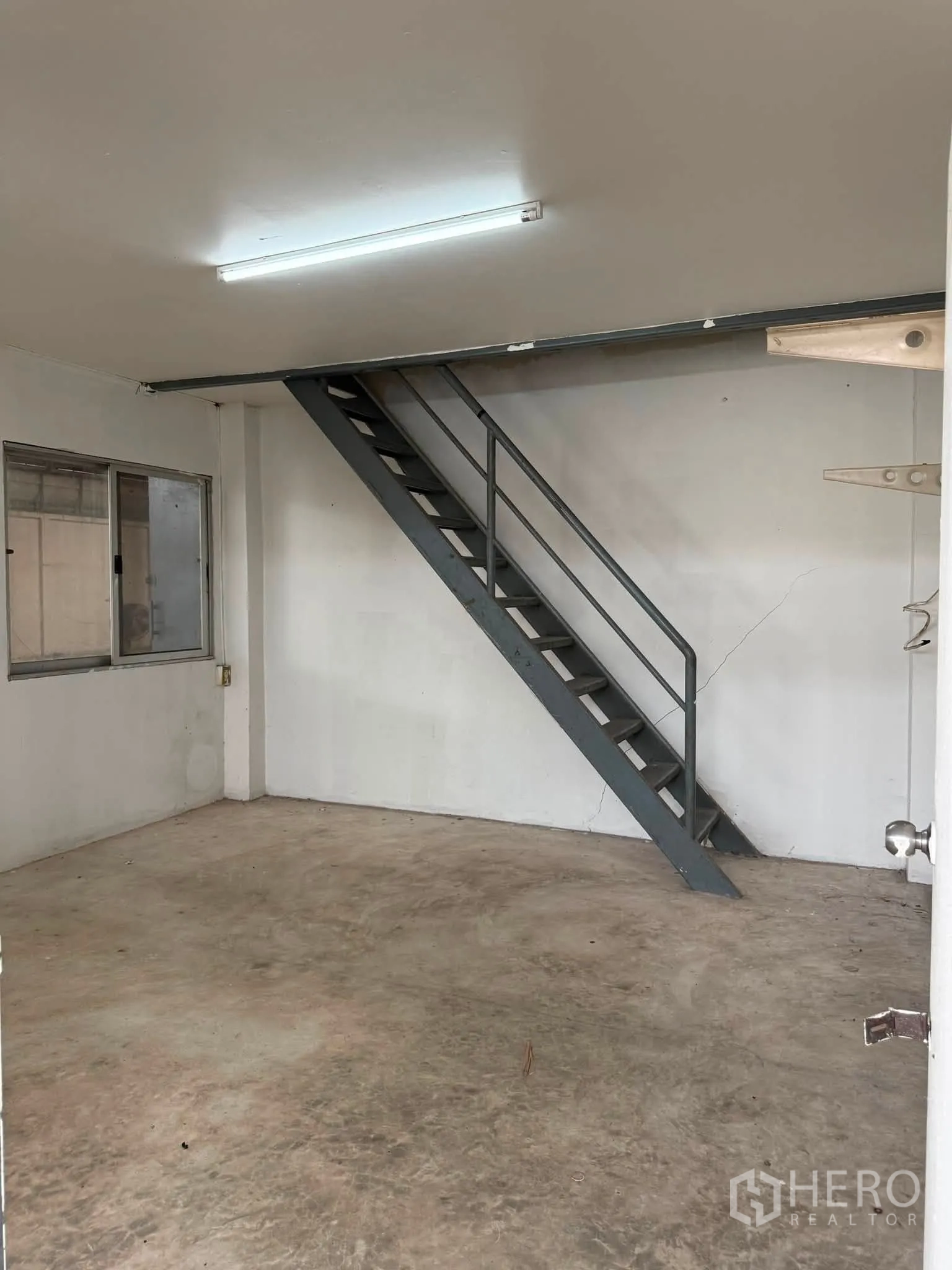 Warehouse for rent or sale in Phra Khanong, Bangkok - Empty room with concrete floor and metal stairs to upper level.