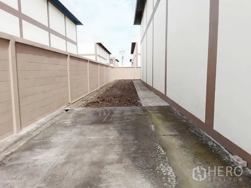 Factory for rent or sale in Pathum Thani - Rear service lane beside warehouse blocks with drainage and concrete paving.