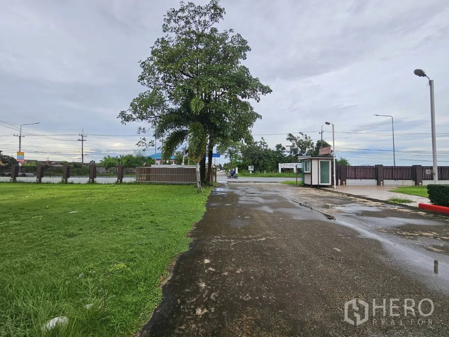 Warehouse for rent in Lam Luk Ka, Pathum Thani - Driveway to front gate with guard booth and green verge.