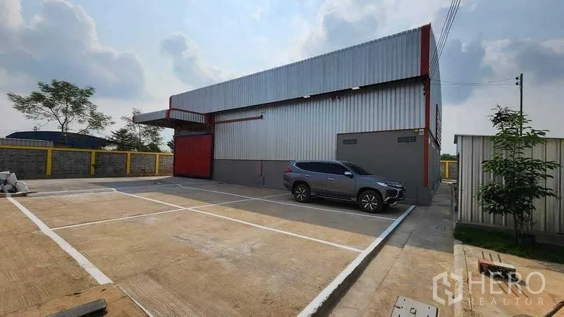 Warehouse for rent in Nong Chok, Bangkok - Exterior parking and loading area beside the metal-clad warehouse with a red roller door.