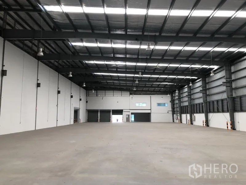 Factory for rent in Bang Sao Thong, Samut Prakan - Expansive factory hall showing multiple roller shutters and mezzanine office windows.